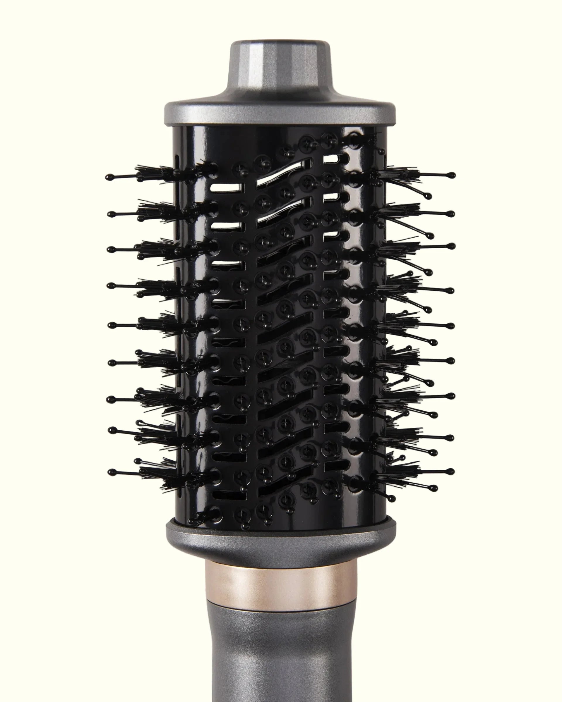 Vista de acercamiento del cabezal cepillo del secador Aerobrush™ de Auralis sobre fondo crema: cilindro negro con múltiples hileras de cerdas negras tipo pin distribuidas en espiral por toda la superficie, tapa superior gris metálico, y en la parte inferior un anillo decorativo rosa dorado antes de la empuñadura gris del cuerpo del secador.