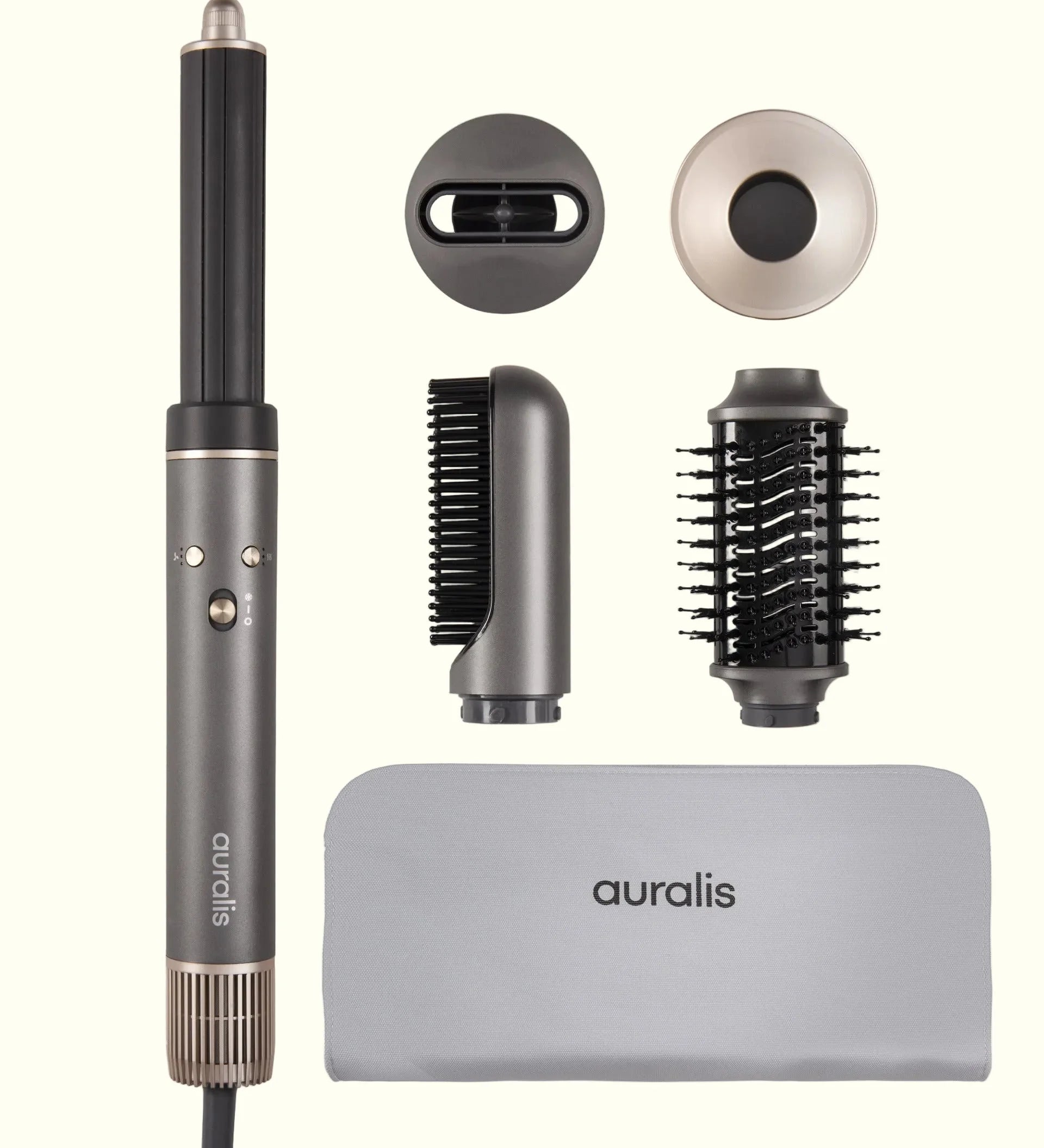Set completo del secador multiestilo Aeroflow™ de Auralis en color gris grafito, fotografiado sobre fondo crema: el cuerpo principal con boquilla difusora redonda a la izquierda; arriba a la derecha dos tapas de accesorio, una ovalada negra y una circular en tono champán; en el centro un cepillo redondo térmico de cerdas negras y un accesorio concentrador de boquilla estrecha; abajo una funda de viaje de tela gris con el logo "auralis" bordado.